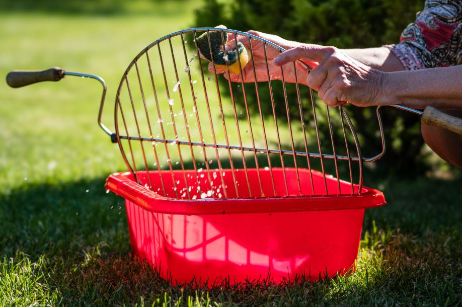 woman scrubbing a charcoal grill grate in soapy water