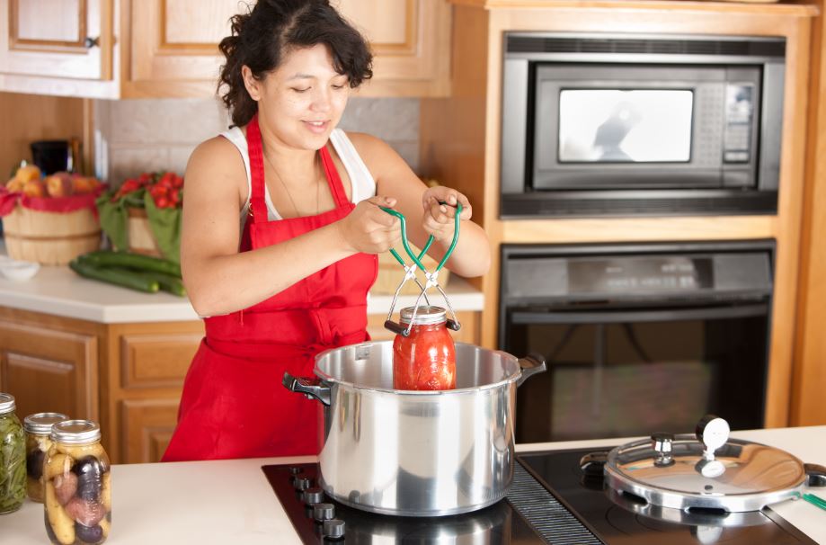 woman putting a jar into a boiling water bath